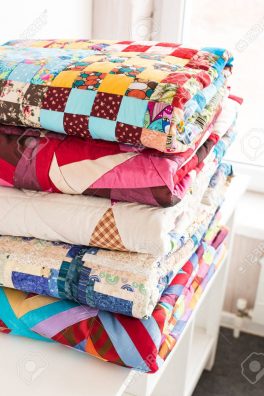 patchwork and fashion concept - beautiful stack of colorful quilts, bedspreads stacked in several rows in height for storage, sale of stitched products on a white background.
